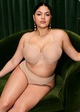 Woman wearing a beige bra and panties set sitting on a green couch.