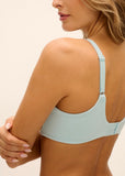 A woman shown from the back wearing a light blue underwire bra with textured cups and adjustable straps against a plain cream background.