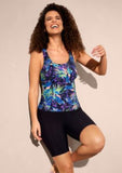 Woman wearing a colorful tank top and black shorts on a beige background