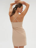 Woman wearing a beige dress with thin straps on a plain background